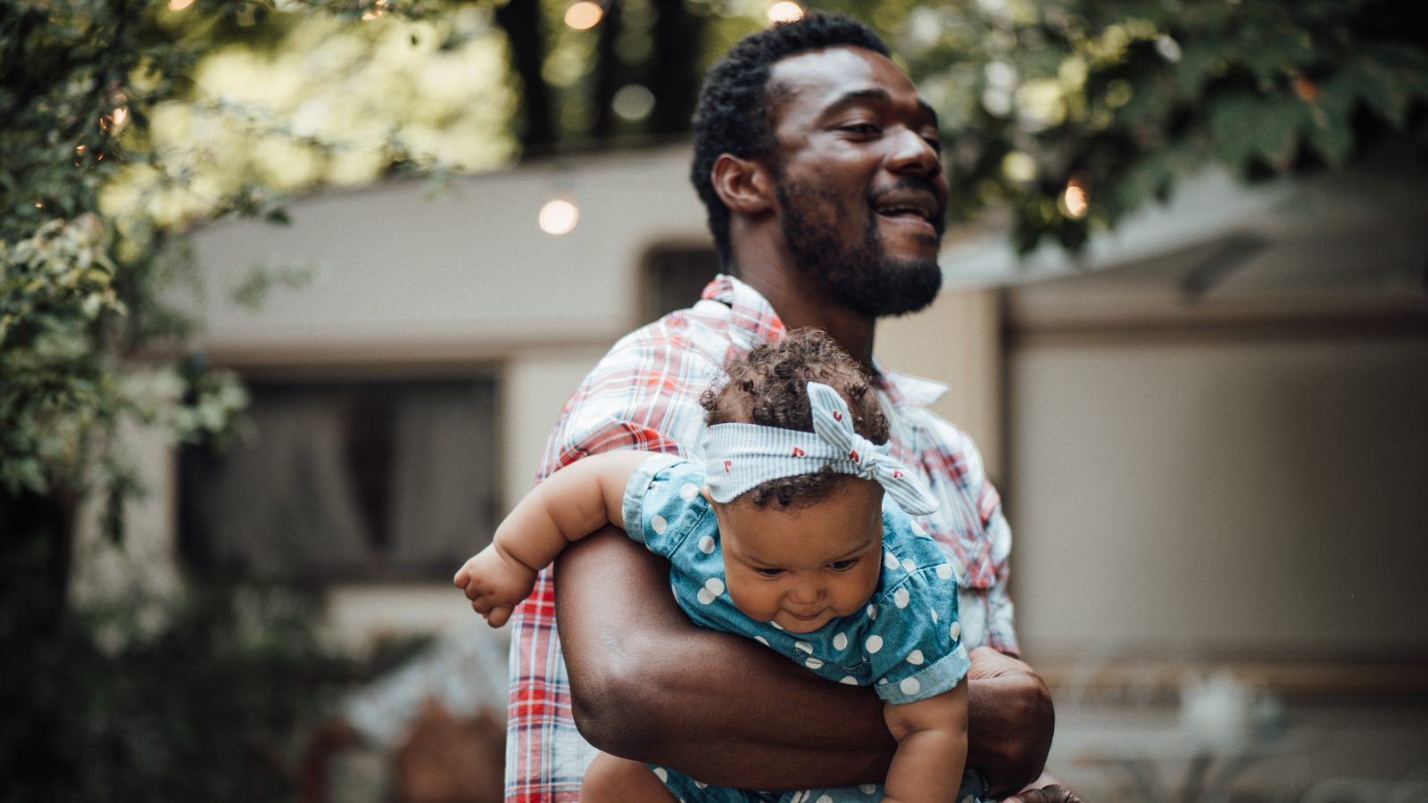 A father carrying his baby daughter on one arm, looking out past her