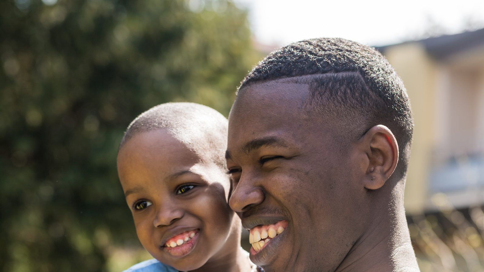 A young father holding his son close, outdoors in the sun