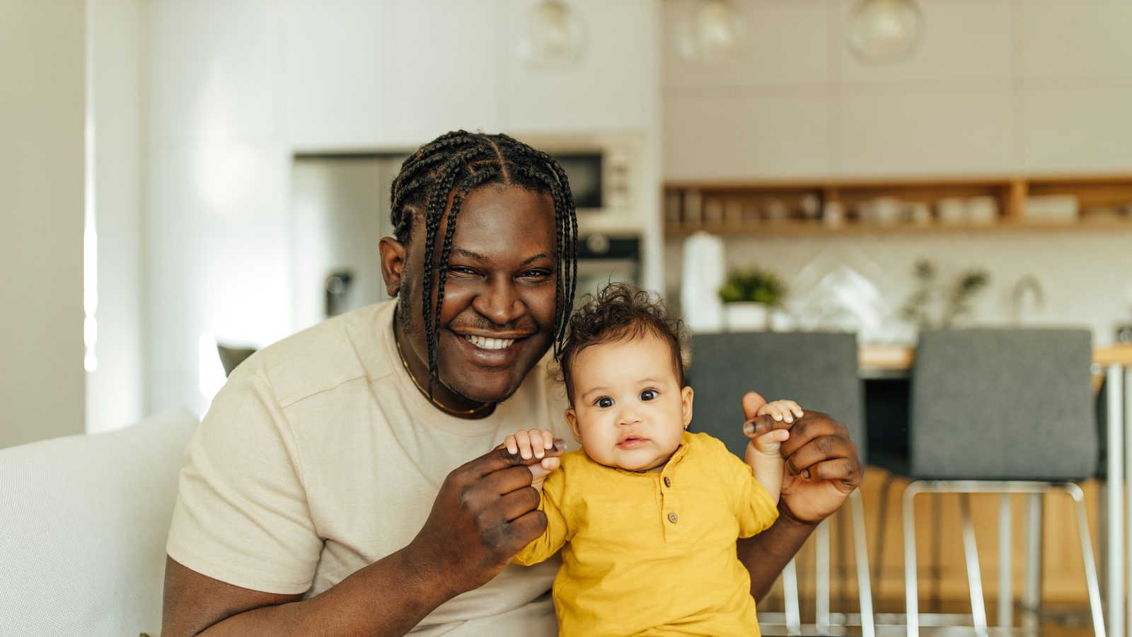 A father sitting at home with his baby son, both of them looking straight ahead