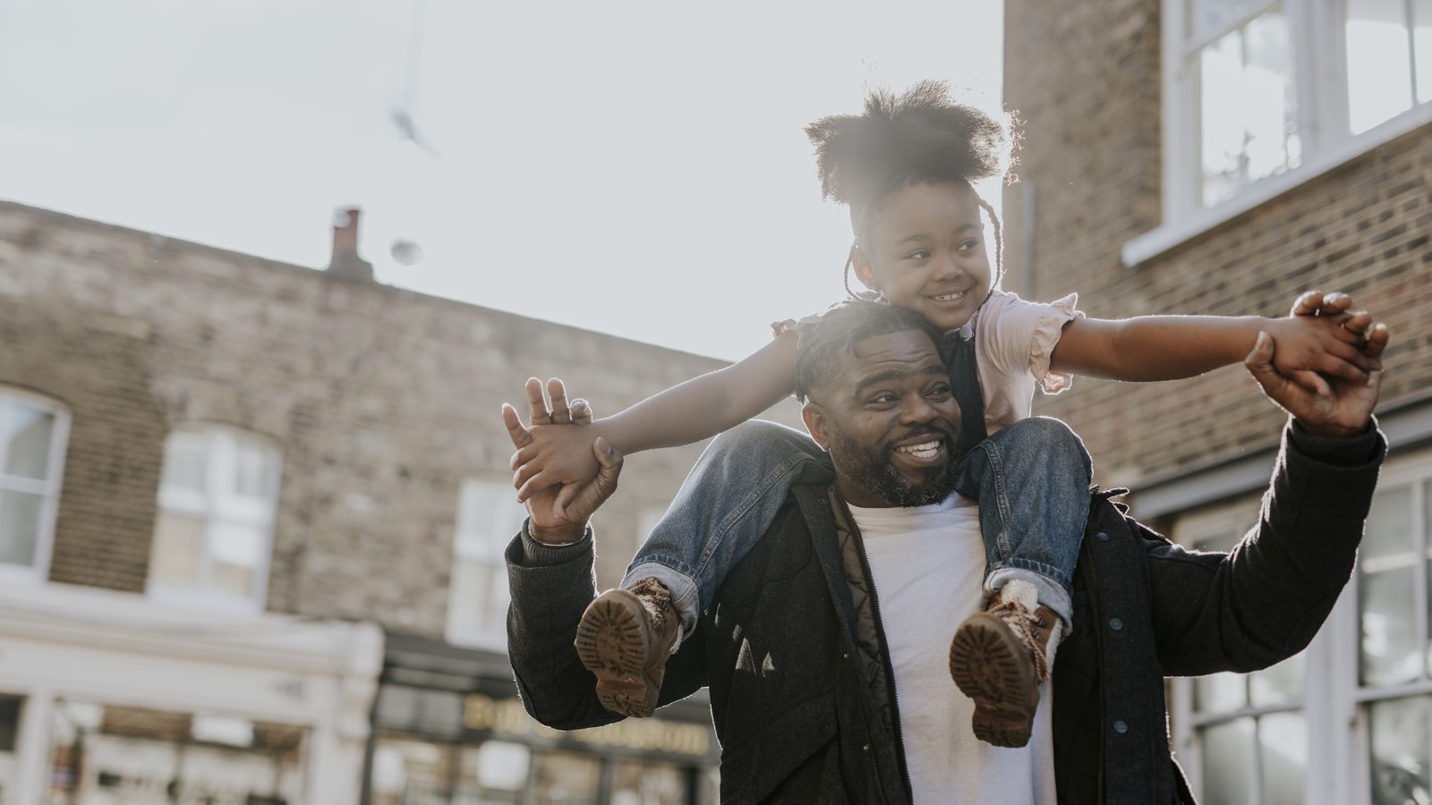 A father walking down a street with his daughter on his shoulders